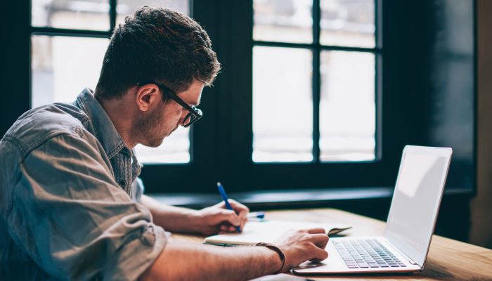 Man using laptop and writing in a journal